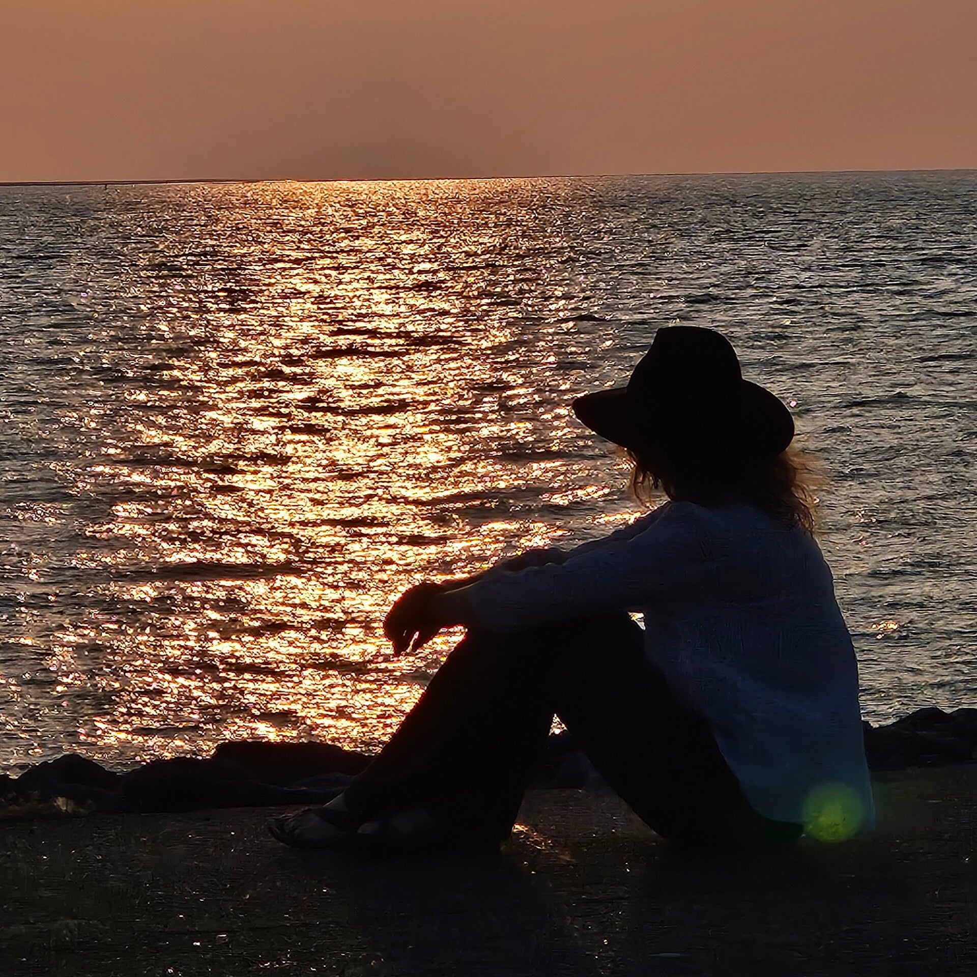 Vrouw zit stil aan het water bij zonsondergang